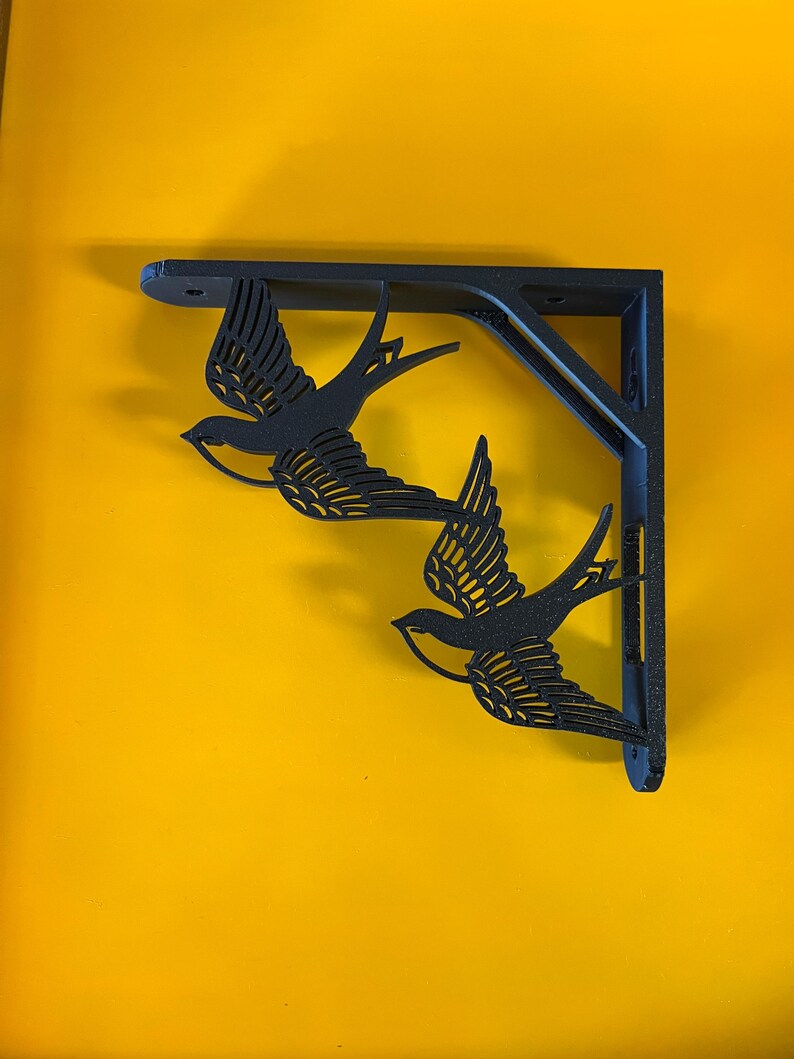 May include: Black metal shelf bracket with a decorative design of two stylized birds in flight.