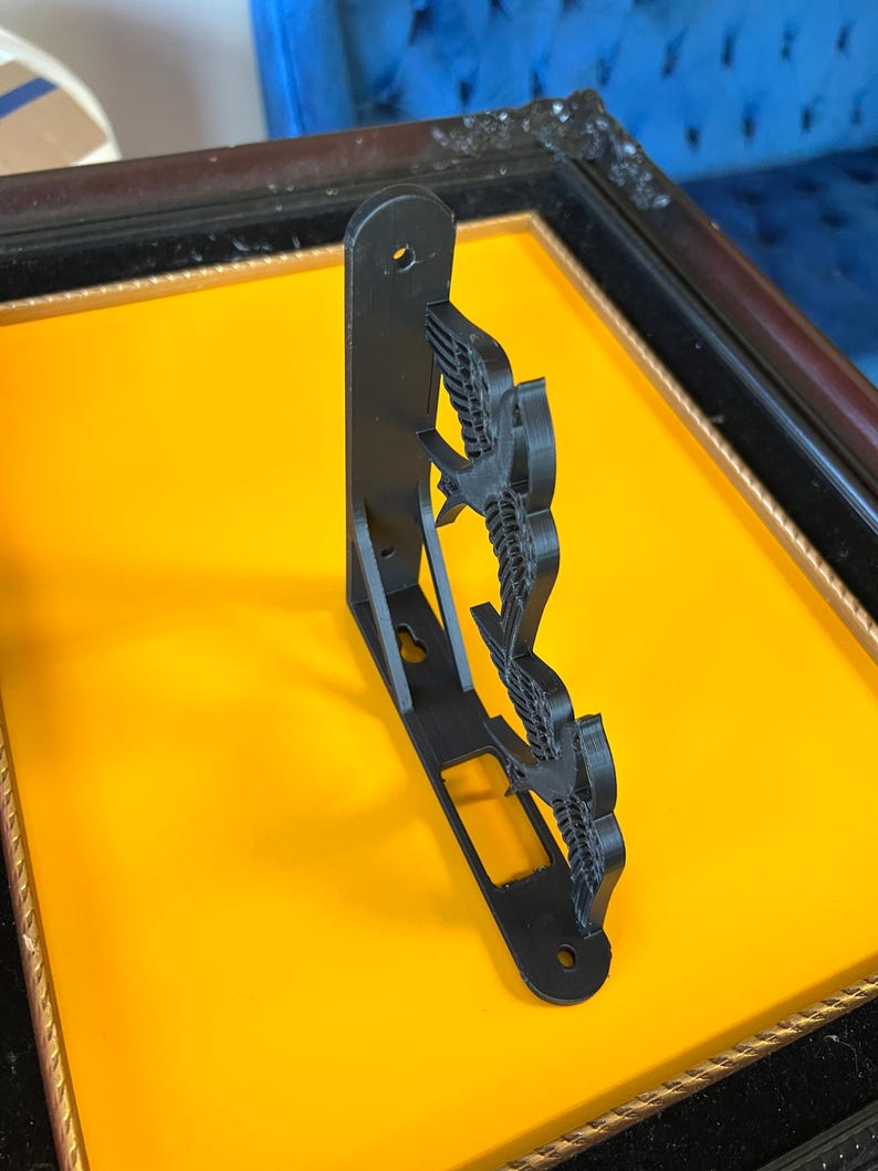 May include: Black metal shelf bracket with a decorative design of three birds in flight. The bracket is mounted on a yellow surface.
