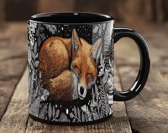May include: Black ceramic mug featuring a sleeping fox illustration. The fox is depicted in shades of brown and orange, nestled among white and gray foliage against a black background. The mug has a black handle and a glossy finish.