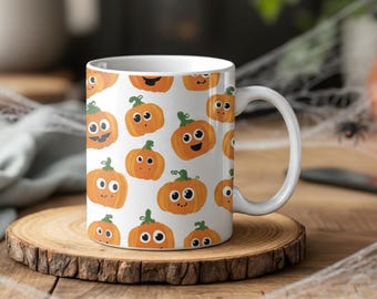 Op de afbeelding: Witte keramische mok met een herhalend patroon van oranje cartoonpompoenen met groene stelen en verschillende gezichtsuitdrukkingen. De mok heeft een wit handvat, perfect voor Halloween.