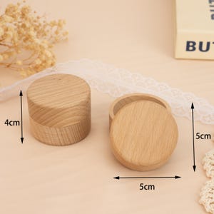 May include: Two wooden boxes with lids, each measuring 5 cm in diameter and 4 cm in height. The boxes are made of light brown wood and have a smooth, polished finish.