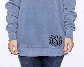 May include: A light blue sweatshirt with a black monogram on the bottom right side. The monogram is a stylized "DSJ".