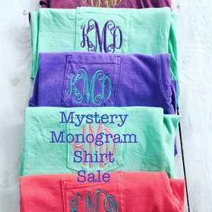 May include: Stack of five t-shirts with different colors and embroidered monograms in the pocket. The text "Mystery Monogram Shirt Sale" is printed on the shirts.