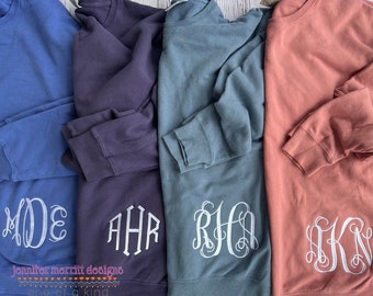 May include: Four sweatshirts in different colors with embroidered monograms. The sweatshirts are blue, purple, teal, and coral. The monograms are white and are in a script font. The text "Jennifer merrit designs one of a kind" is at the bottom of the image.