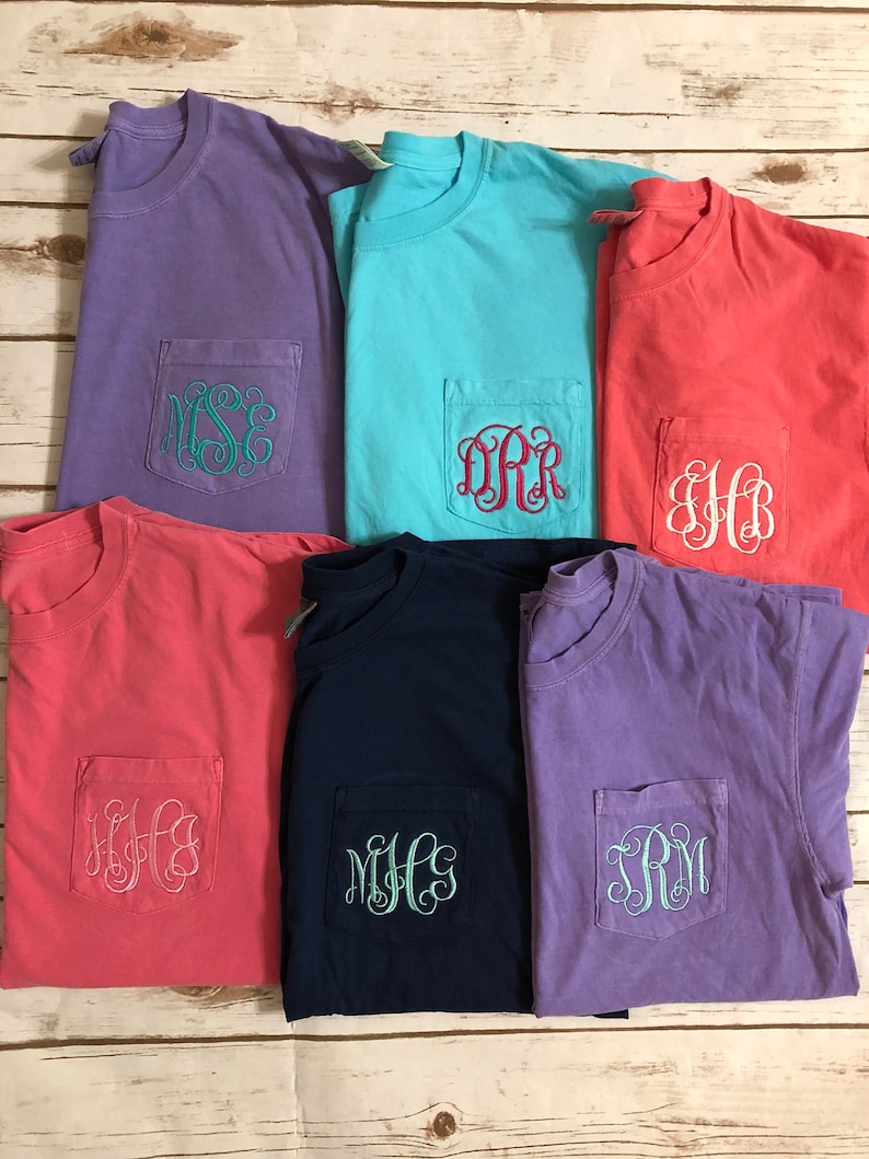 May include: Six t-shirts with different colors and monograms embroidered on the pocket. The colors are purple, light blue, coral, pink, navy blue, and lavender. The monograms are "MSE", "DRR", "HB", "KFG", "MHC", and "SRM".