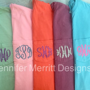 May include: Five different colored t-shirts with a pocket on the front. Each pocket has a different monogram embroidered on it. The monograms are in different colors. The text "Jennifer Merritt Designs" is at the bottom of the image.