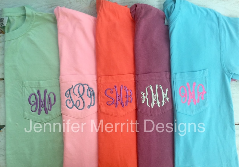May include: Five different colored t-shirts with a pocket on the front. Each pocket has a different monogram embroidered on it. The monograms are in different colors. The text "Jennifer Merritt Designs" is at the bottom of the image.