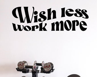 May include: Black weightlifting equipment in a home gym. A cable machine with a pull-down bar, a weight rack with dumbbells, and a weight bench with the text "Wish less work more" on the wall.