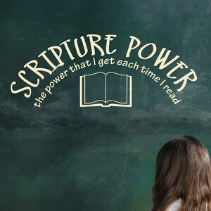May include: A young girl sits in front of a green chalkboard with the words "Scripture Power the power that I get each time I read" written on it. She is looking up at the chalkboard, and a teddy bear sits on the floor in front of her.