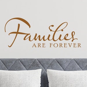 May include: A gray sofa with two white pillows and a black side table with a silver teapot and a white cup. The wall behind the sofa has a brown vinyl decal that reads "Families are forever."