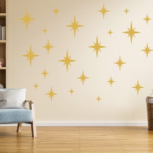 Puede incluir: Un interior de sala de estar con un sillón azul claro, una estantería de madera con la palabra "LOVE" escrita en bloques rosas y una pared decorada con pegatinas de pared en forma de estrella dorada.