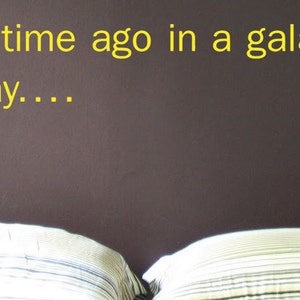 May include: A dark brown headboard with a white and yellow inscription that reads "A long time ago in a galaxy far, far away..." Two white and grey striped pillows are on the bed.