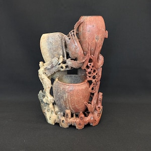 Può includere: Una scultura in pietra scolpita con tre vasi di diverse dimensioni e forme. La scultura è intagliata in modo intricato con motivi di draghi e uccelli ed è principalmente nelle tonalità del rosso, beige e grigio. La base è un design dettagliato e strutturato.