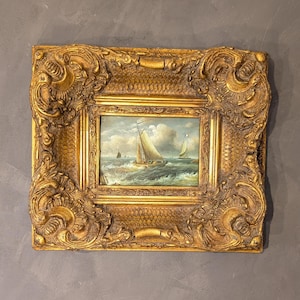 May include: An antique oil painting of sailboats on the sea, set in a heavily ornate, gold-colored frame. The painting depicts several sailboats on a choppy sea under a cloudy sky. The frame has intricate, swirling details.