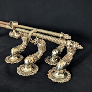 Könnte beinhalten: Satz von vier Gardinenstangenhaltern aus Messing mit Drachendesign. Die Halter haben einen geschwungenen, schlangenartigen Körper und eine kreisförmige Basis mit dekorativem Rand. Die Stangen sind goldfarben.