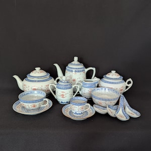 May include: A porcelain tea set with a blue and white floral pattern. The set includes teapots, cups, saucers, a creamer, a sugar bowl, a bowl, and spoons. The tea set has a traditional Asian design.