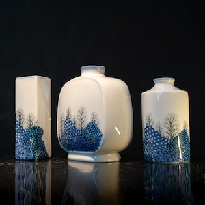 May include: Three white ceramic vases with blue and green floral designs. The vases are of different shapes and sizes.