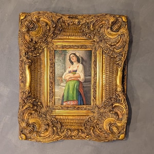 May include: Ornate gold-colored framed painting. The painting depicts a woman in traditional attire, with a white blouse, green skirt, and colorful accents. The frame has intricate, detailed carvings.