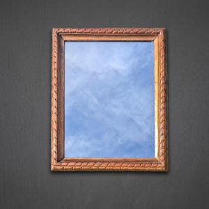 Peut inclure: Un miroir mural rectangulaire doté d'un cadre en bois brun moyen avec une texture sculptée en forme de corde sur les bords. La surface en verre réfléchissant affiche un ciel bleu clair avec des nuages blancs, créant un effet visuel lumineux.
