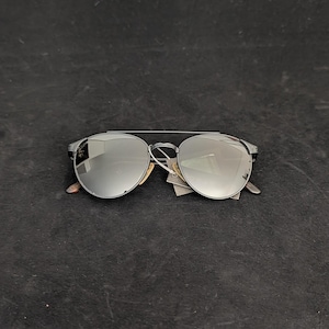 May include: Silver-framed aviator sunglasses with reflective lenses. The sunglasses have a double bridge and a dark gray frame. The lenses are round and reflect the surrounding environment. The sunglasses are new and have a tag attached.