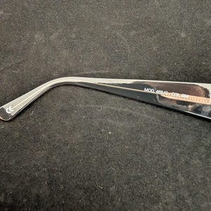 Puede incluir: Primer plano de una patilla de gafas plateada y negra. La patilla tiene el texto "MOD 468/G COL 684" impreso. La patilla es curva y tiene una marca CE.