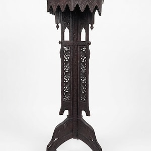 May include: A dark brown, intricately carved wooden plant stand. The stand features a square top with a decorative edge, supported by a detailed column and a three-legged base. The stand is approximately 102 cm tall.