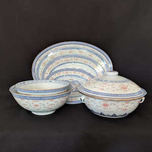 May include: A set of porcelain serving dishes with a blue and coral floral design. The set includes two bowls, a large platter, and a lidded serving dish with gold trim. The dishes are arranged on a black surface.
