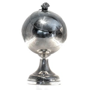 Op de afbeelding: Een zilverkleurige, bolvormige asbak met een scharnierend deksel en een decoratieve bekroning. De asbak is gemonteerd op een voetstuk. Het ontwerp is vintage en elegant, geschikt voor een klassiek of antiek decor.