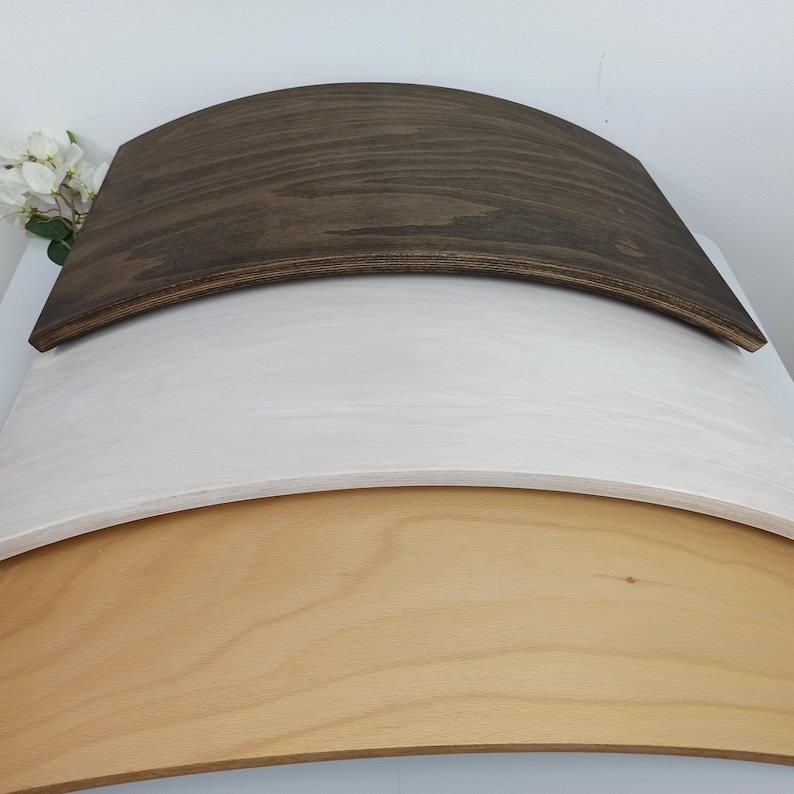 May include: Three curved wooden boards stacked vertically. The top board is dark brown, the middle board is white, and the bottom board is a natural light tan wood color. Each board features a smooth, arched surface with visible wood grain.