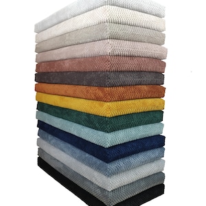 Può includere: Una pila di campioni di tessuto quadrati in vari colori, tra cui bianco, grigio, rosa, marrone, arancione, giallo, verde, blu e nero. Il tessuto ha un aspetto strutturato e intrecciato. I campioni sono ben disposti, mostrando una gamma di tonalità.