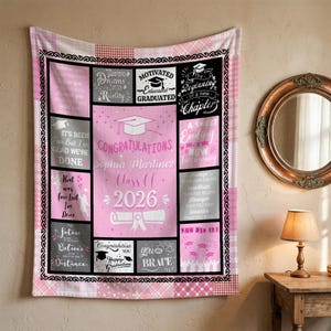 May include: A pink and white graduation blanket with a patchwork design. The blanket features text blocks with phrases like "Congratulations," "Class of 2026," and "Dreams into Reality." A graduation cap and diploma are also featured.