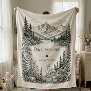 May include: Cream-colored blanket featuring a black and white mountain and lake landscape design. The blanket includes the names "David & Susan" and the date "January 23, 2026". The design is framed by floral and tree illustrations.
