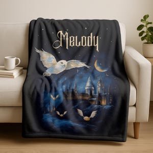 May include: A black throw blanket with a fantasy design. It features a white owl in flight, a castle, and the name "Melody" in a stylized font. The design includes a crescent moon, stars, and flying golden snitches.