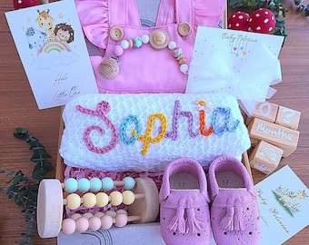 May include: A baby gift set in a box, featuring a pink romper, a white towel embroidered with the name "Sophia", and a pair of pink leather shoes. Includes a wooden abacus, wooden blocks, and greeting cards. The set is designed for a baby.