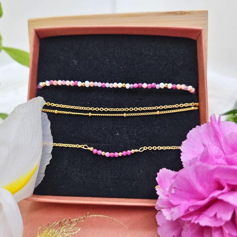 May include: Three delicate gold chain bracelets with small beads, one with pink beads, one with multi-coloured beads, and one with a single row of pink beads.