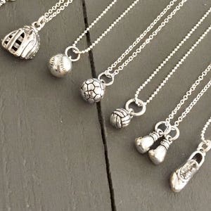 May include: A collection of silver necklaces with various sports-themed charms, including a baseball bat, baseball glove, baseball, soccer ball, basketball, boxing gloves, and a shoe.