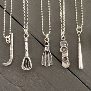 May include: Ten silver necklaces with various sports-themed charms, including a hockey stick, lacrosse stick, baseball bat, scuba flippers, a catcher's mitt, a soccer ball, a baseball, and boxing gloves.