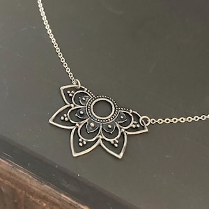 May include: A silver chain necklace with a black mandala pendant. The pendant is a detailed design of a flower with a circle in the centre.