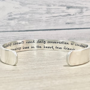 May include: Silver cuff bracelet with an engraved message: "Friendship doesn't need daily conversation or constant contact. Friendship lives in the heart, true friends..."