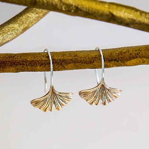 Könnte beinhalten: Ein Paar silberne Ohrhänger mit goldenen Ginkgoblatt-Anhängern. Die Blätter haben ein detailliertes, strukturiertes Design.