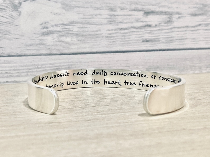 May include: Silver cuff bracelet with an engraved message: "Friendship doesn't need daily conversation or constant contact. Friendship lives in the heart, true friends..."
