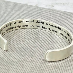 May include: Silver cuff bracelet with an engraved message: "Friendship doesn't need daily conversation or constant contact, the relationship lives in the heart, true friends will..."