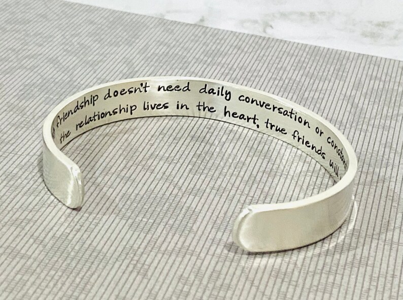 May include: Silver cuff bracelet with an engraved message: "Friendship doesn't need daily conversation or constant contact, the relationship lives in the heart, true friends will..."
