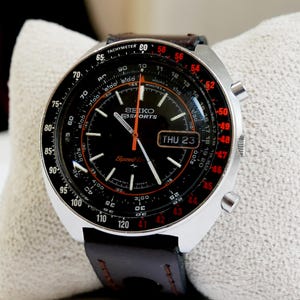 May include: A vintage Seiko Sports watch with a black dial, featuring a tachymeter bezel and a brown leather strap. The watch has a silver-tone case and displays the day as Thursday 23. The watch face includes orange and white accents.