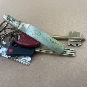 以下が含まれることがあります： キーホルダーに付いた鍵のコレクション。鍵は様々な形とサイズがあり、真鍮の鍵と「59-73 УВРГМ 9340」と書かれた金属製のタグが付いた鍵が含まれています。赤いキーフォブと黒い鍵もあります。