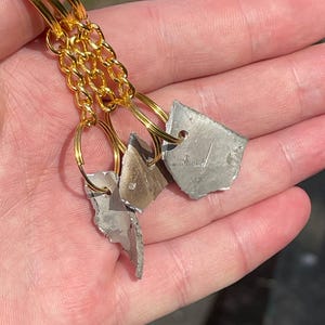 May include: Gold-toned bracelet with three irregular, gray-silver pendants. The pendants are connected to the bracelet with gold-colored hoops and a chain. The bracelet is made of multiple gold bands.