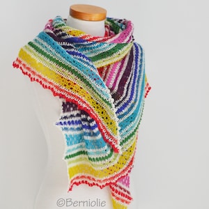 Può includere: Uno scialle fatto a mano dai colori dell'arcobaleno, esposto su un manichino. Presenta strisce rosse, gialle, verdi, blu e viola. I bordi sono rifiniti con un bordo rosso smerlato. Lo scialle ha una forma triangolare.