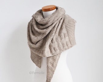 May include: A beige knitted shawl with a textured pattern. The shawl is draped over a white mannequin.