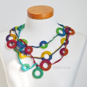 Op de afbeelding: Een veelkleurige gehaakte ketting met grote, kleurrijke cirkels. De ketting is gemaakt van garen in tinten rood, oranje, geel, groen, blauw en paars.