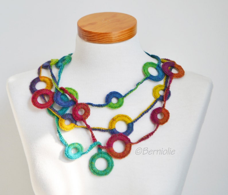 Op de afbeelding: Een veelkleurige gehaakte ketting met grote, kleurrijke cirkels. De ketting is gemaakt van garen in tinten rood, oranje, geel, groen, blauw en paars.
